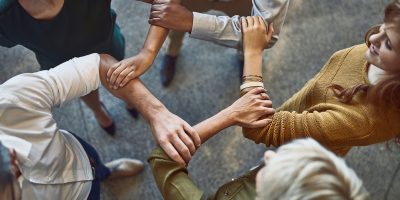 High angle shot of a group of colleagues linking arms in solidarity at work.