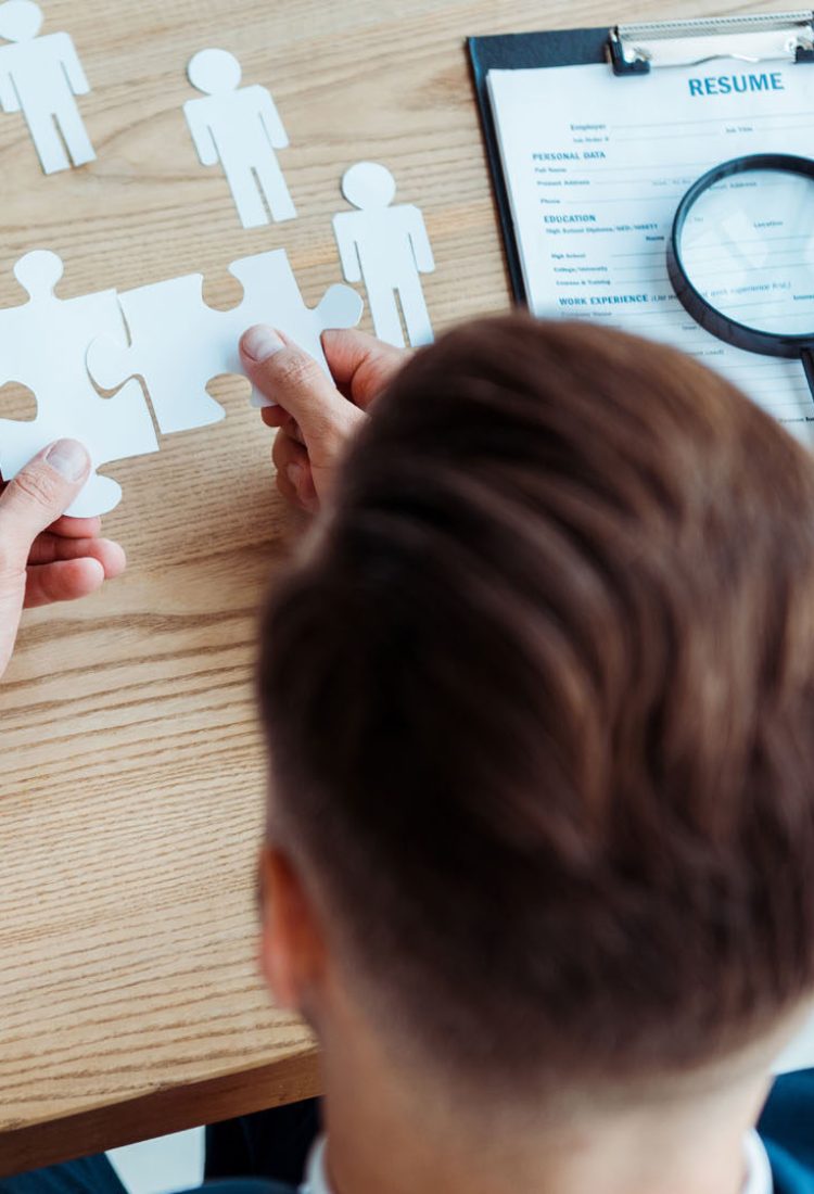 cropped view of man holding jigsaw puzzle pieces near table