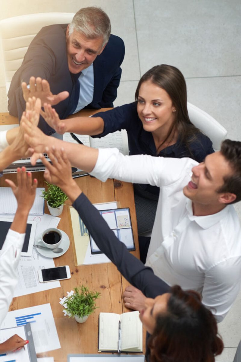 High angle shot of a group of businesspeople high fiving together in an office.