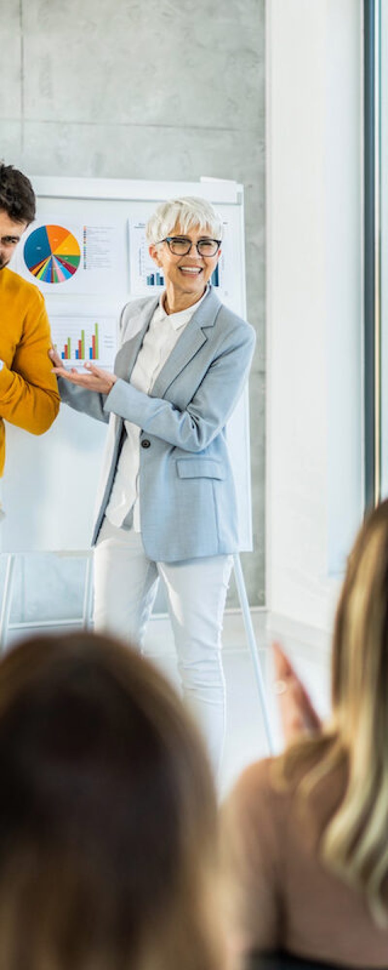 Happy senior businesswoman introducing a new young member of a company to a group of business people. Business people congratulating a applauding to young man for job well done! Young man being introduced to his new colleagues.