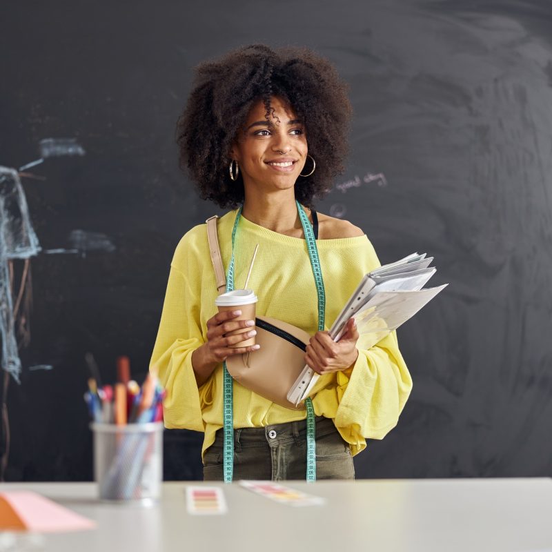 Smiling African-American teacher stands at table against blackboard with drawn human figure at